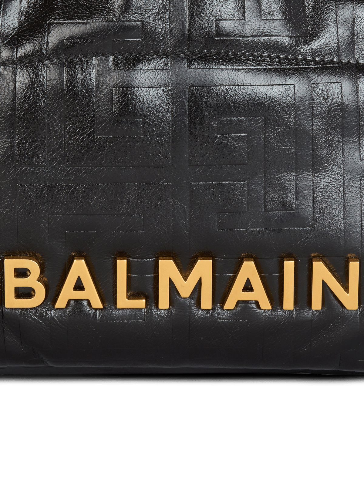 Macro of the gold BALMAIN lettering over the embossed PB labyrinth monogram