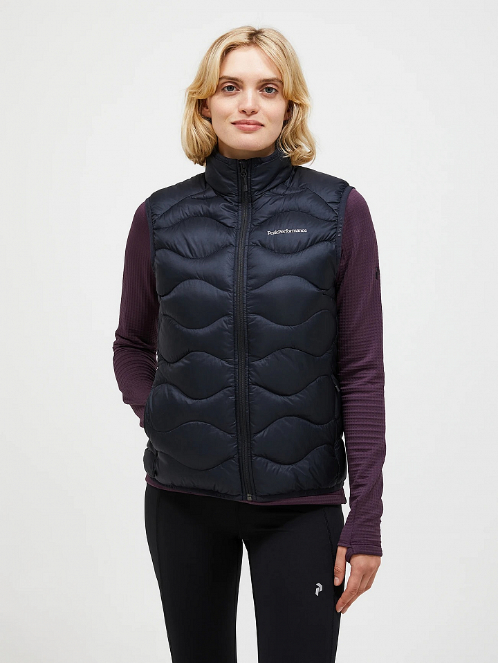 Person wearing a black quilted zip-up puffer vest with a high collar, over a dark purple long-sleeve top and black leggings, front view.