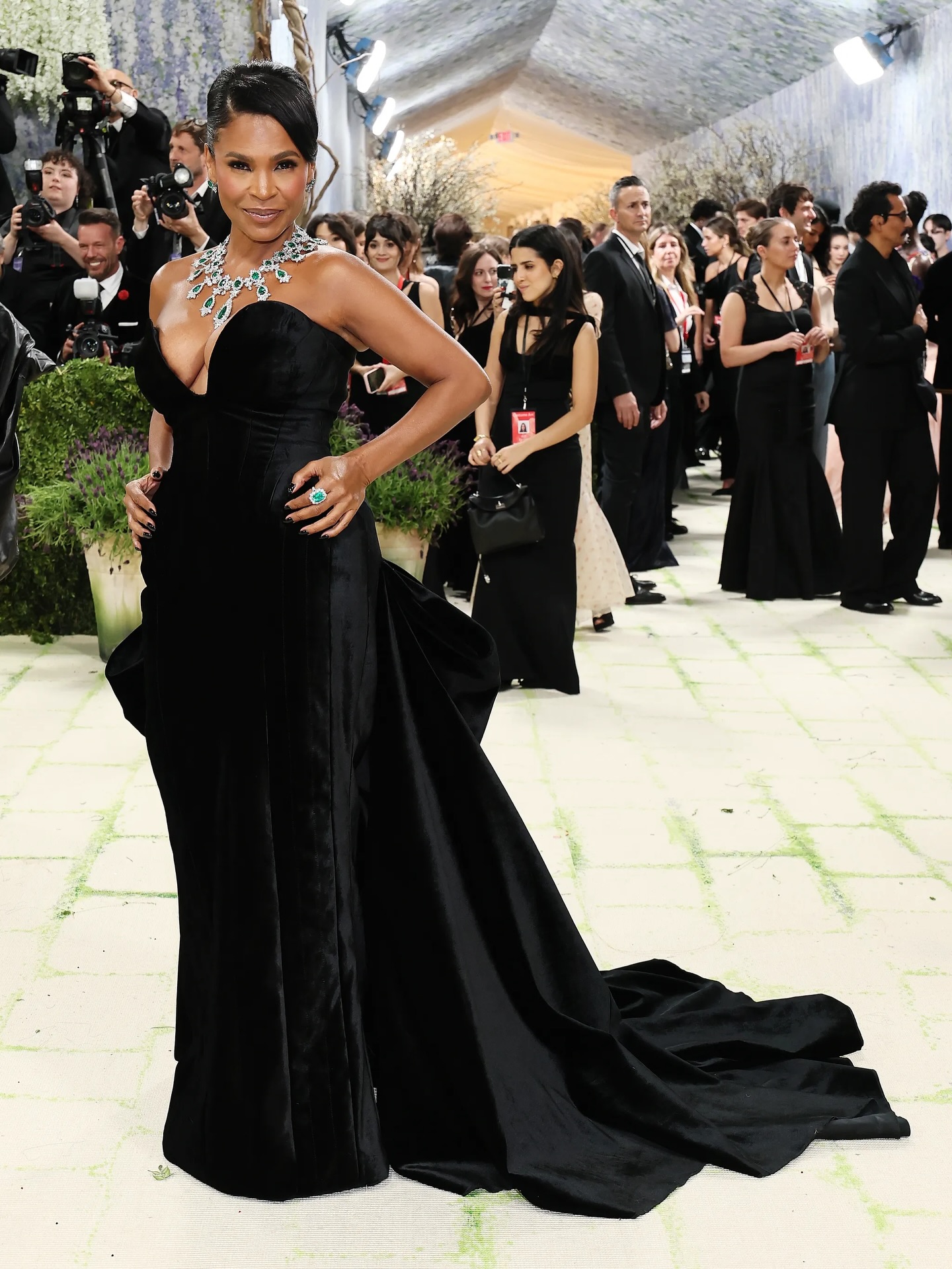 Full-length black gown with sculptural hip volume and a long train on a red carpet