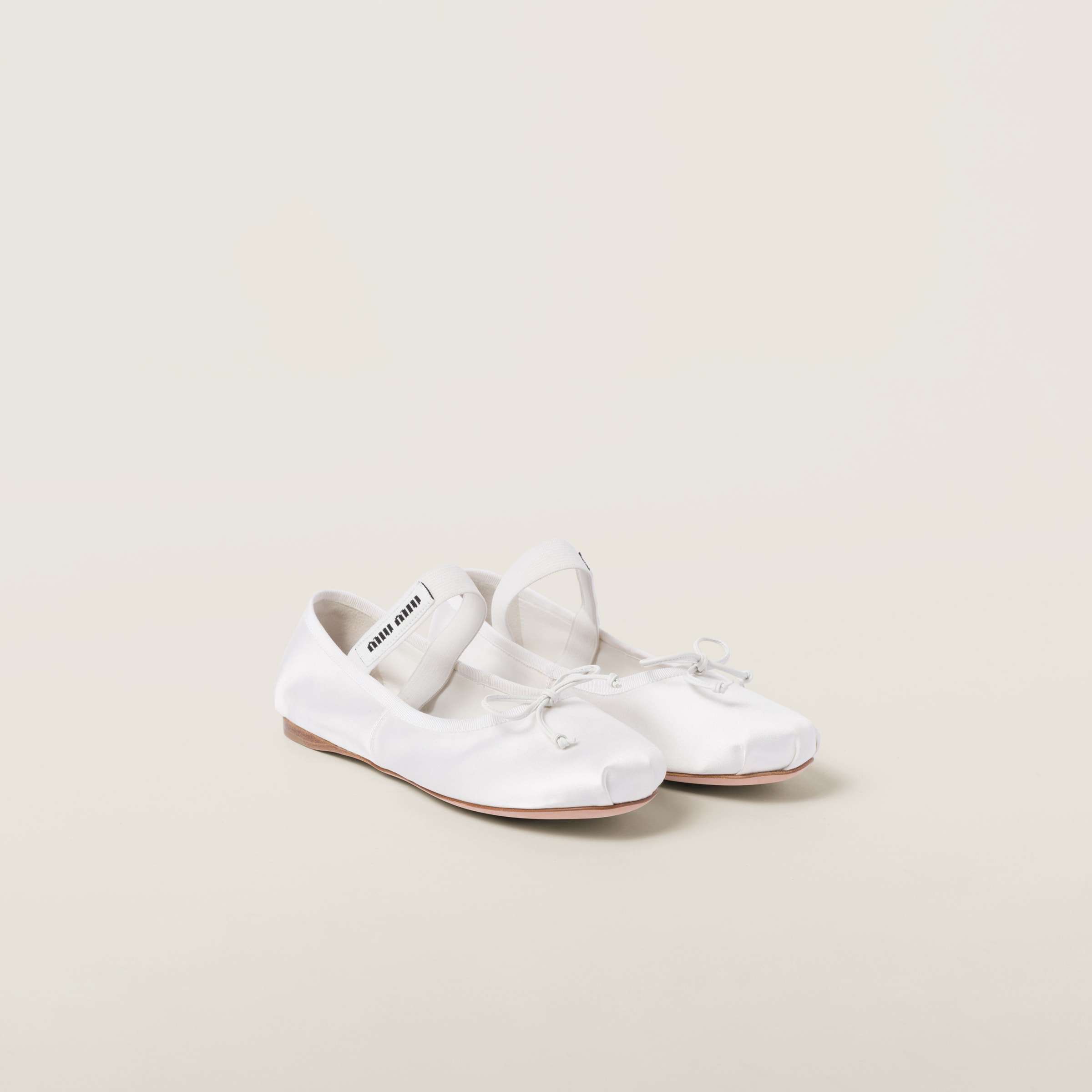 White Miu Miu satin ballerinas with bow, elastic, and knit logo label visible.
