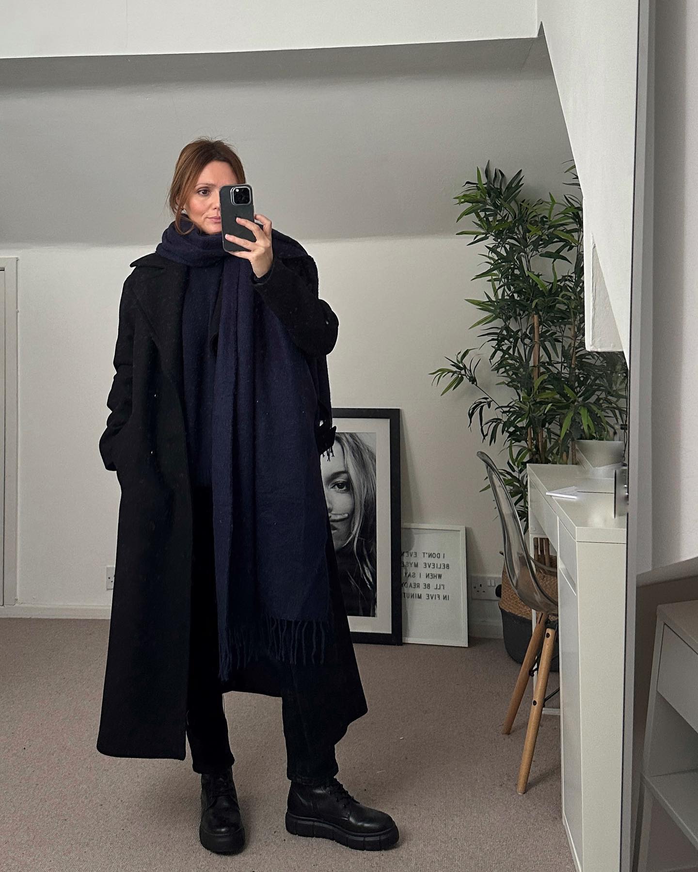 Woman in a navy scarf with a long black coat, black trousers, and black boots