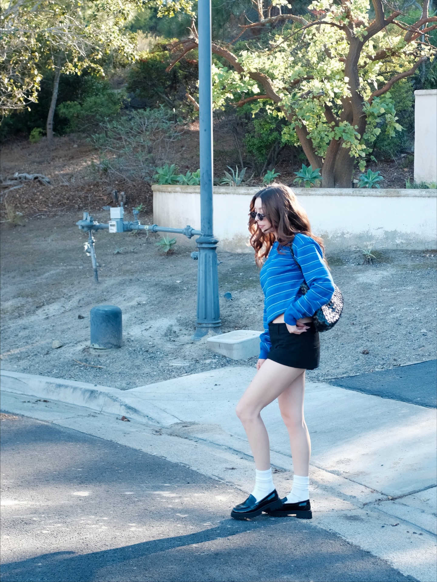 Blue striped sweater, black mini skirt, white socks, and black loafers worn outdoors