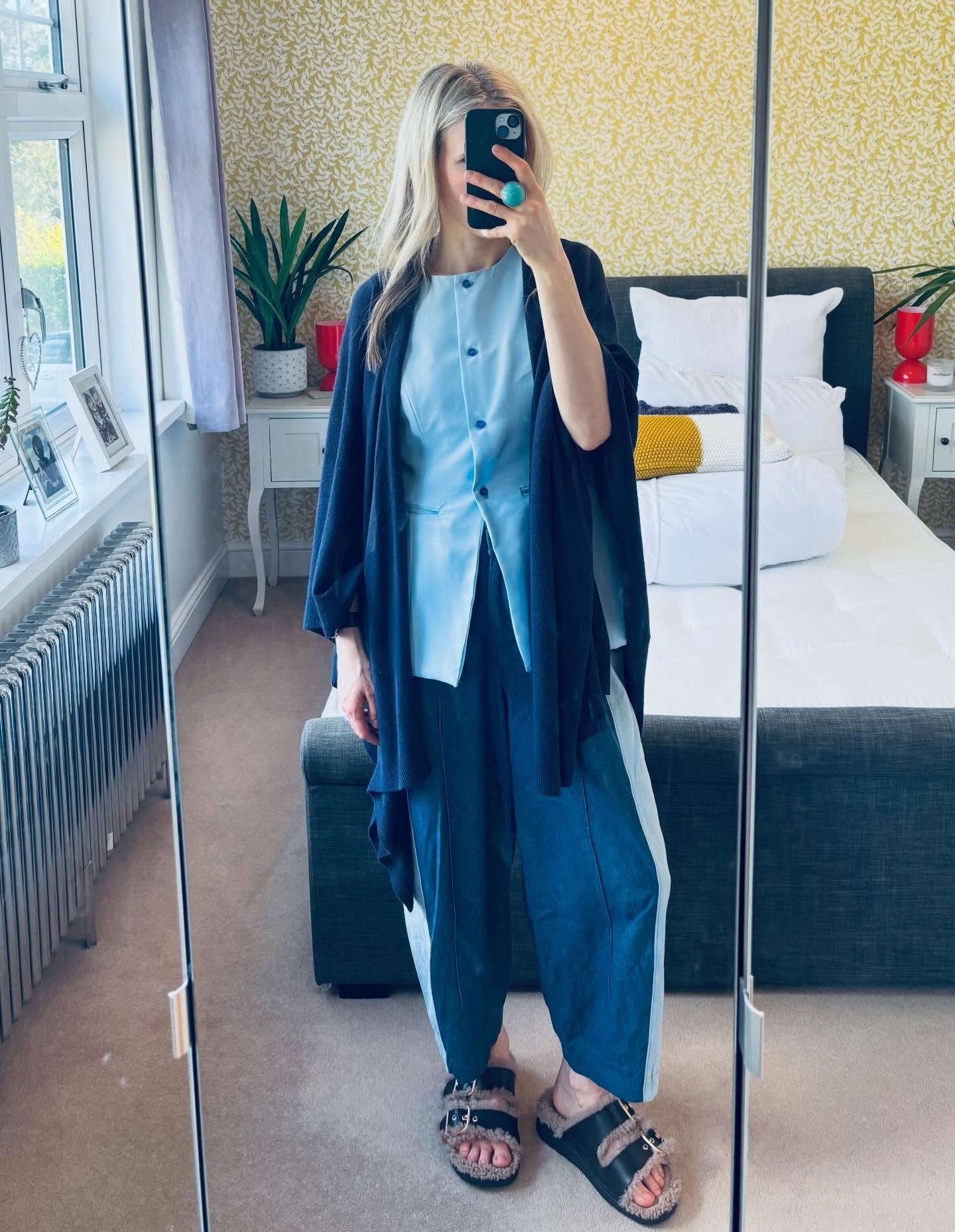 Woman in a light-blue vest with a dark-blue draped layer and wide trousers