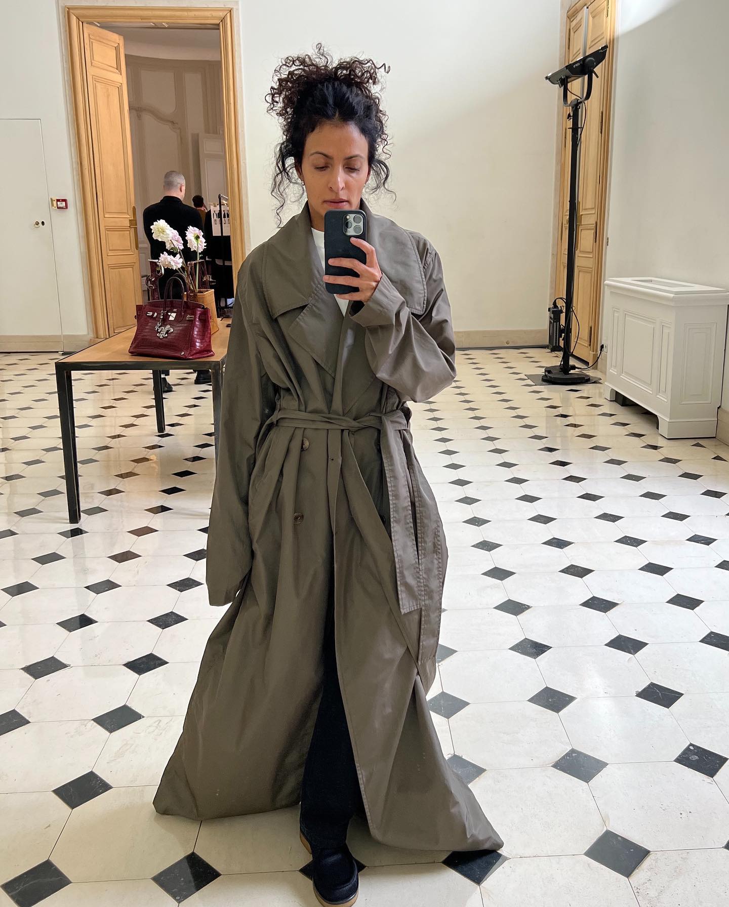 Woman wearing The Row's long belted neutral Cadel coat in a showroom