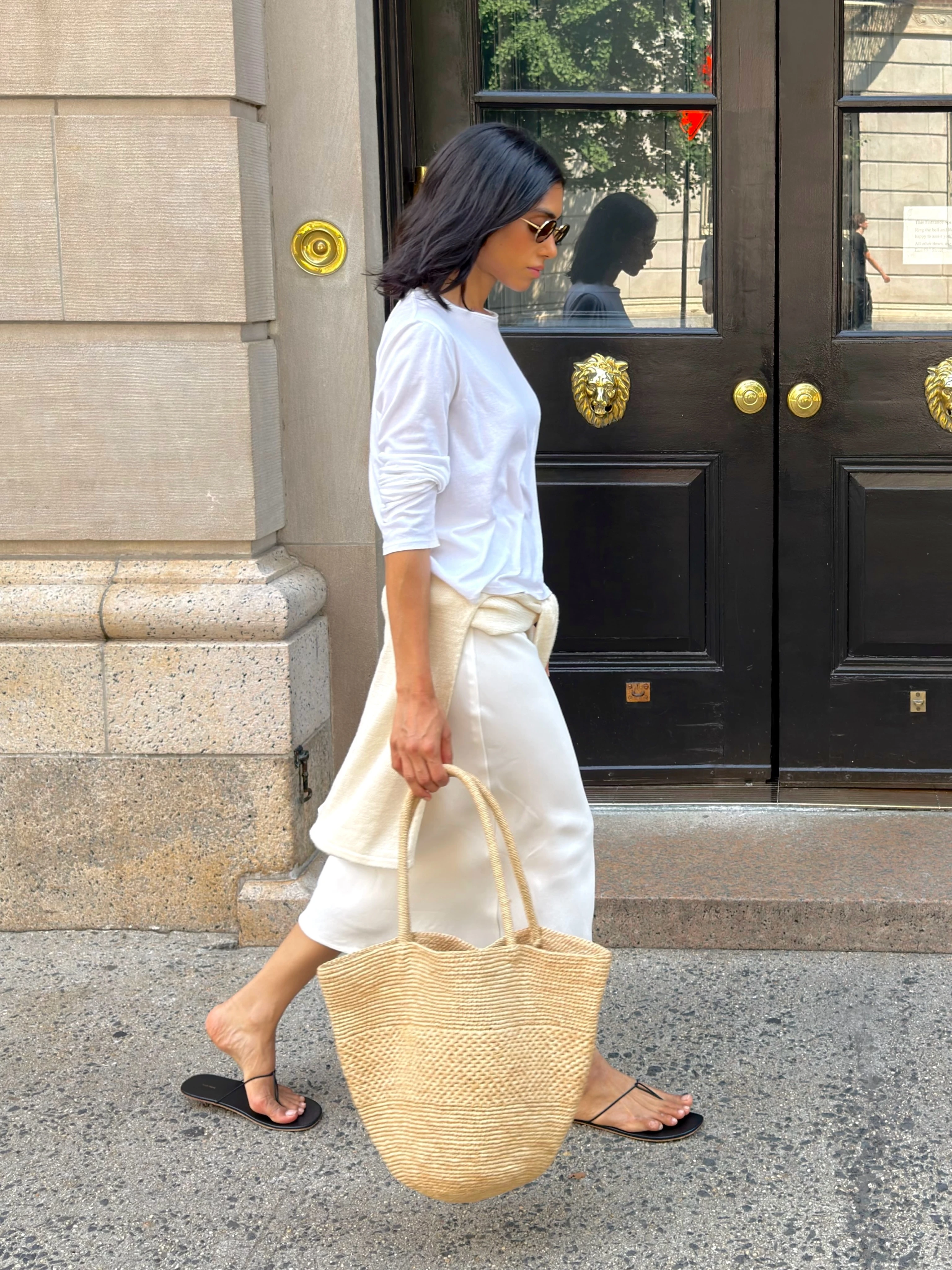 Personal stylist in a complete white outfit carrying a woven tote outdoors