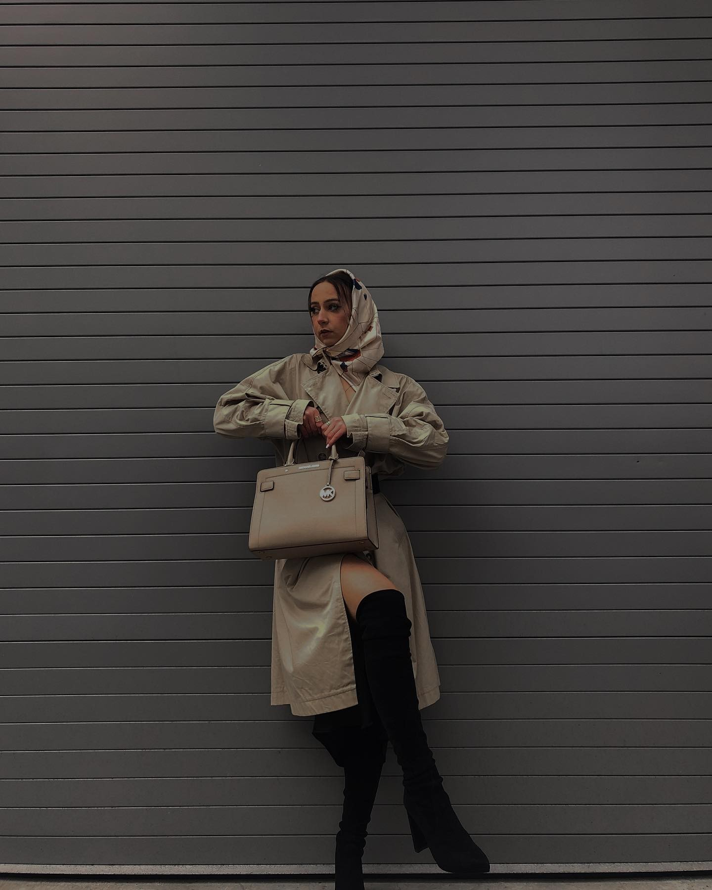 Sonia Gavrilova wears a patterned silk scarf over her hair with a beige trench coat and black over-the-knee boots
