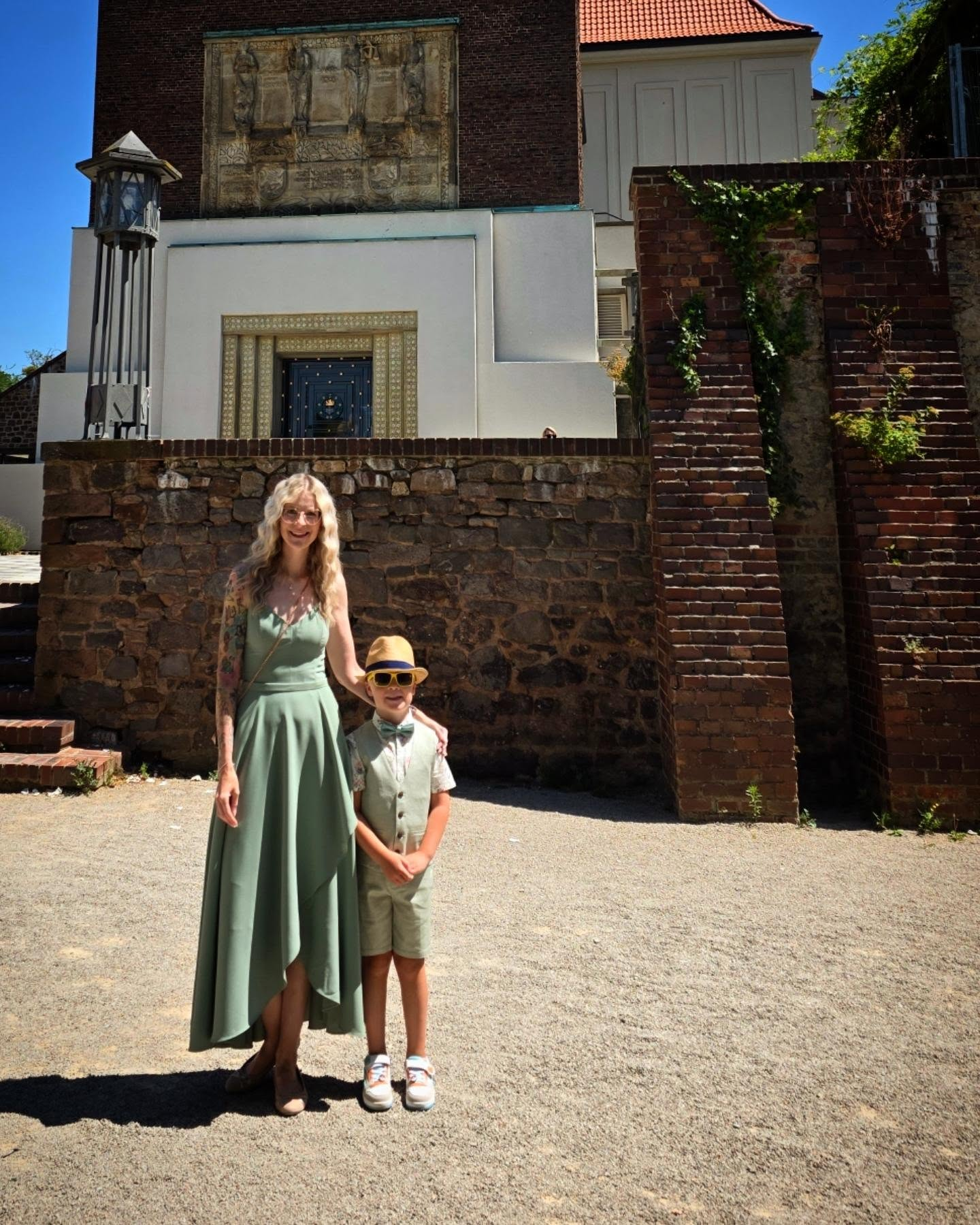 Wedding guest in a sage-green asymmetrical dress and pumps with her son