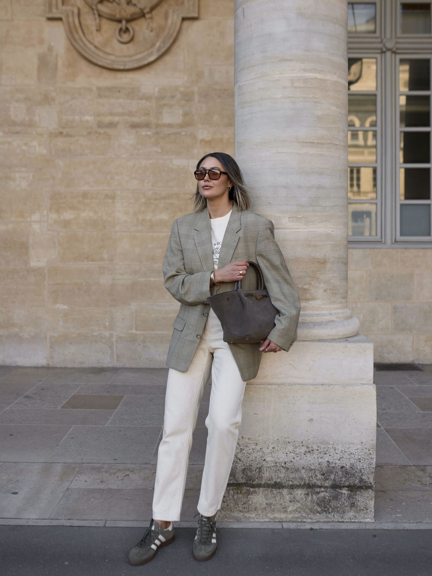 A digital creator in an oversized checked blazer, straight white trousers, dark sneakers, and a structured handbag