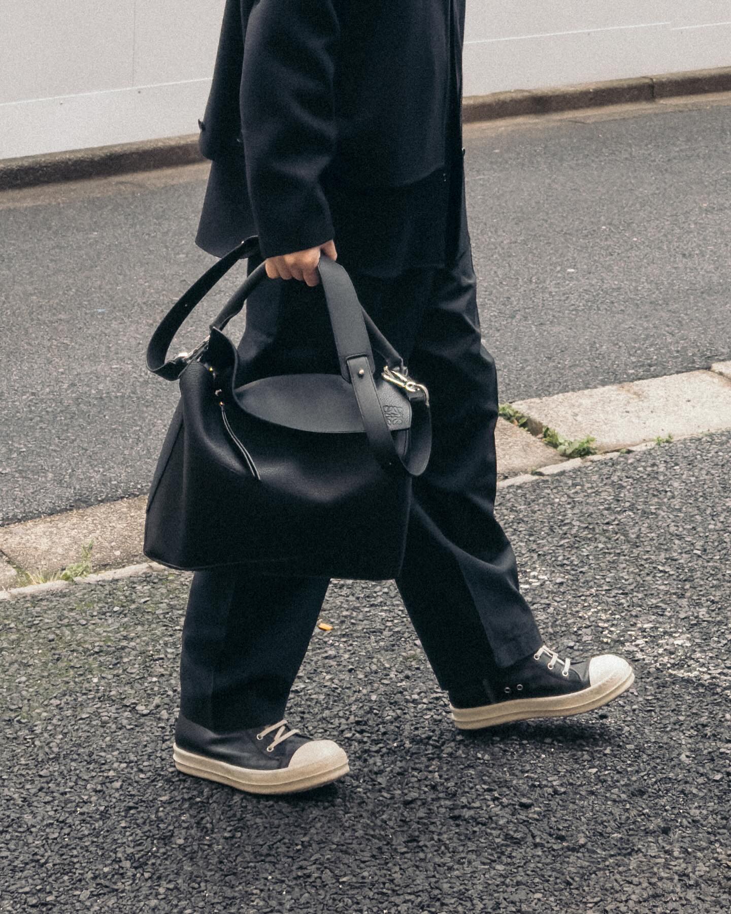 Black Loewe Puzzle bag carried by hand with a black outfit and canvas sneakers