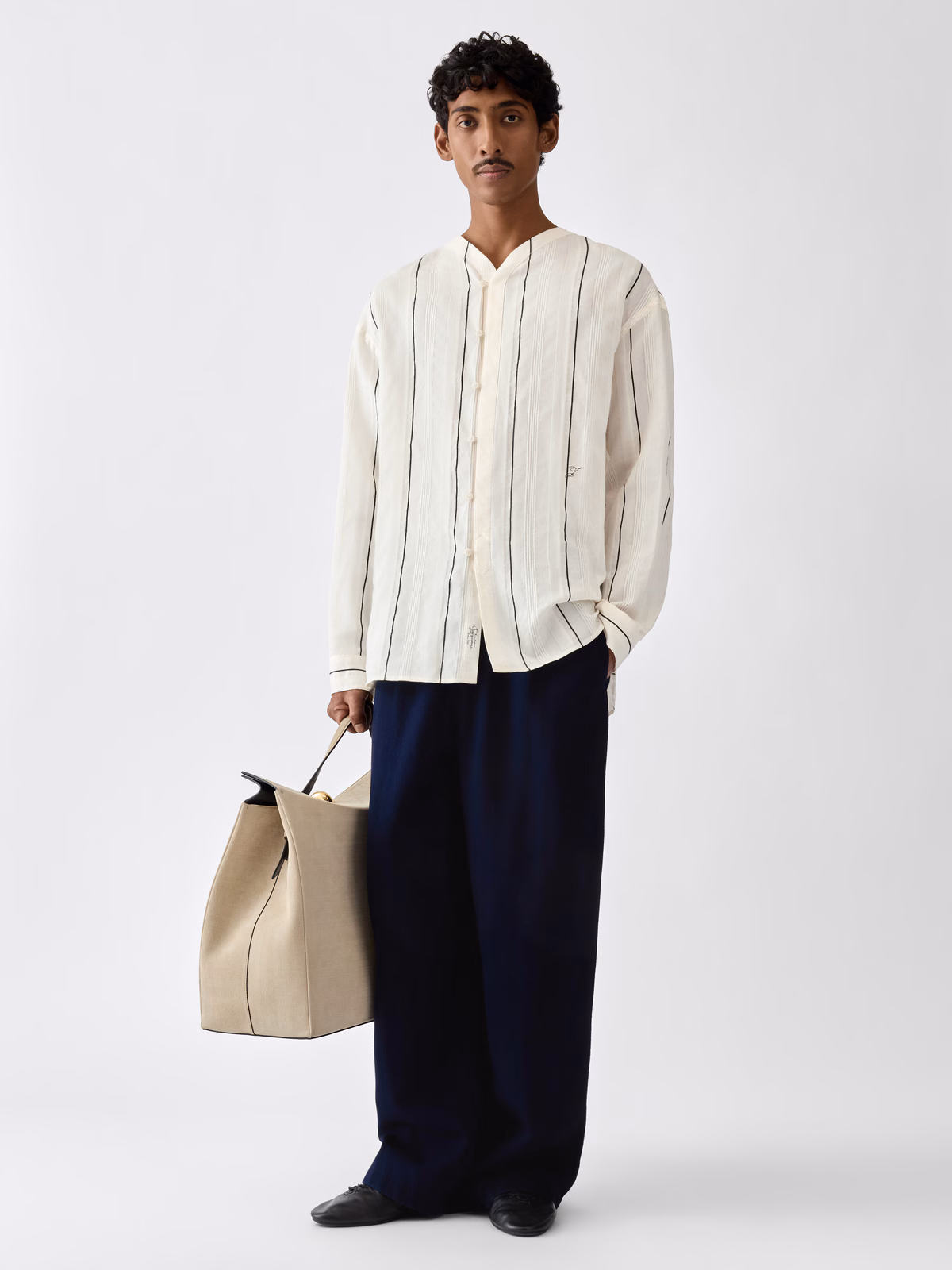 Model wearing Jacquemus The Venice shirt in Stripe White Black with dark trousers and a tote.
