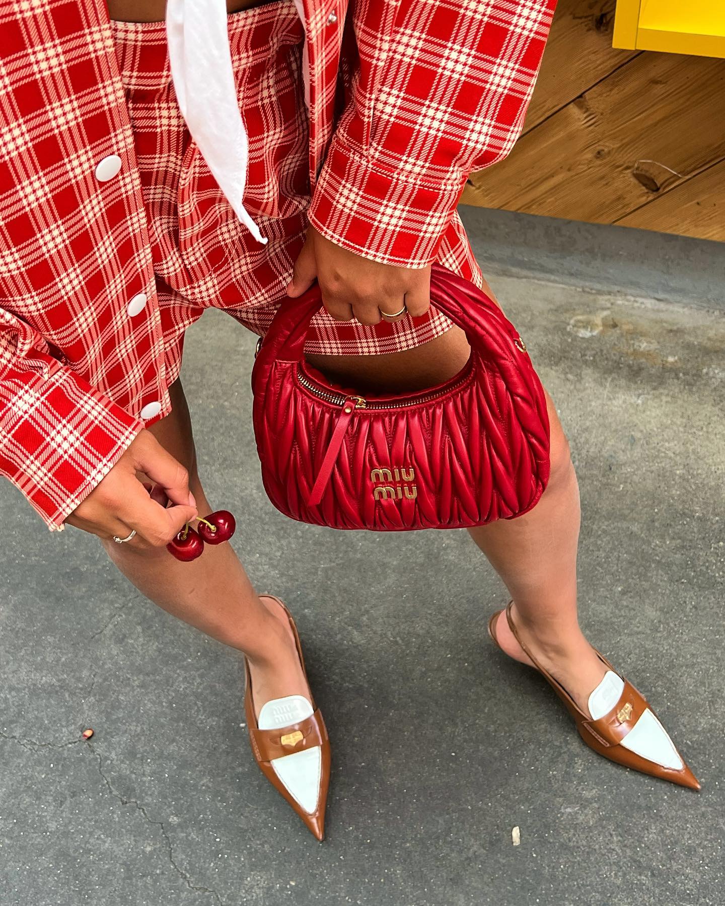 Close view of a red Miu Miu Wander bag held with pointed shoes for capacity and texture reference