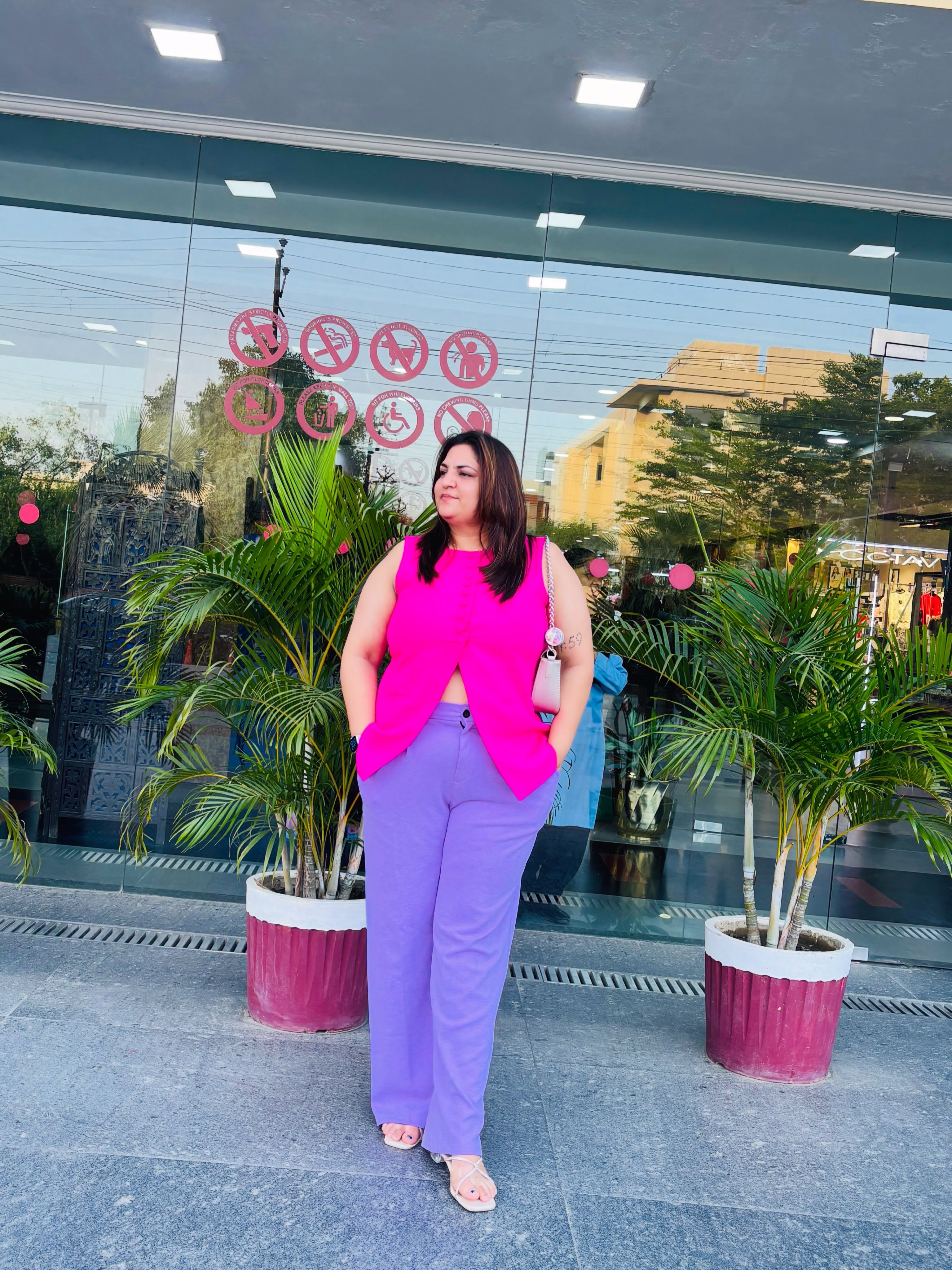 Creator @arising.punjaban wearing a hot-pink sleeveless vest and lavender wide-leg trousers with white sandals