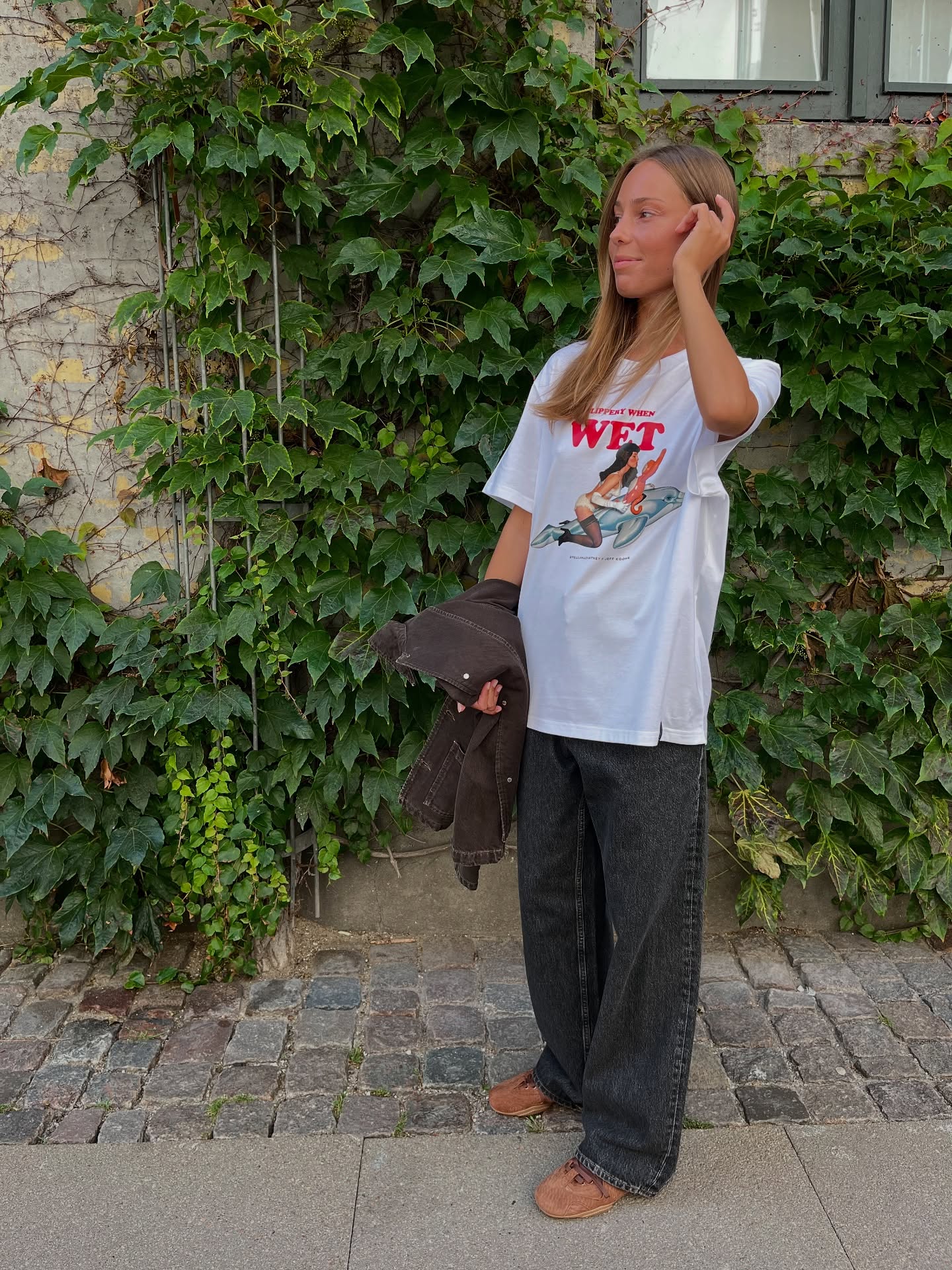 Woman styling wide dark jeans and Acne Studios sneakers with a white graphic T-shirt