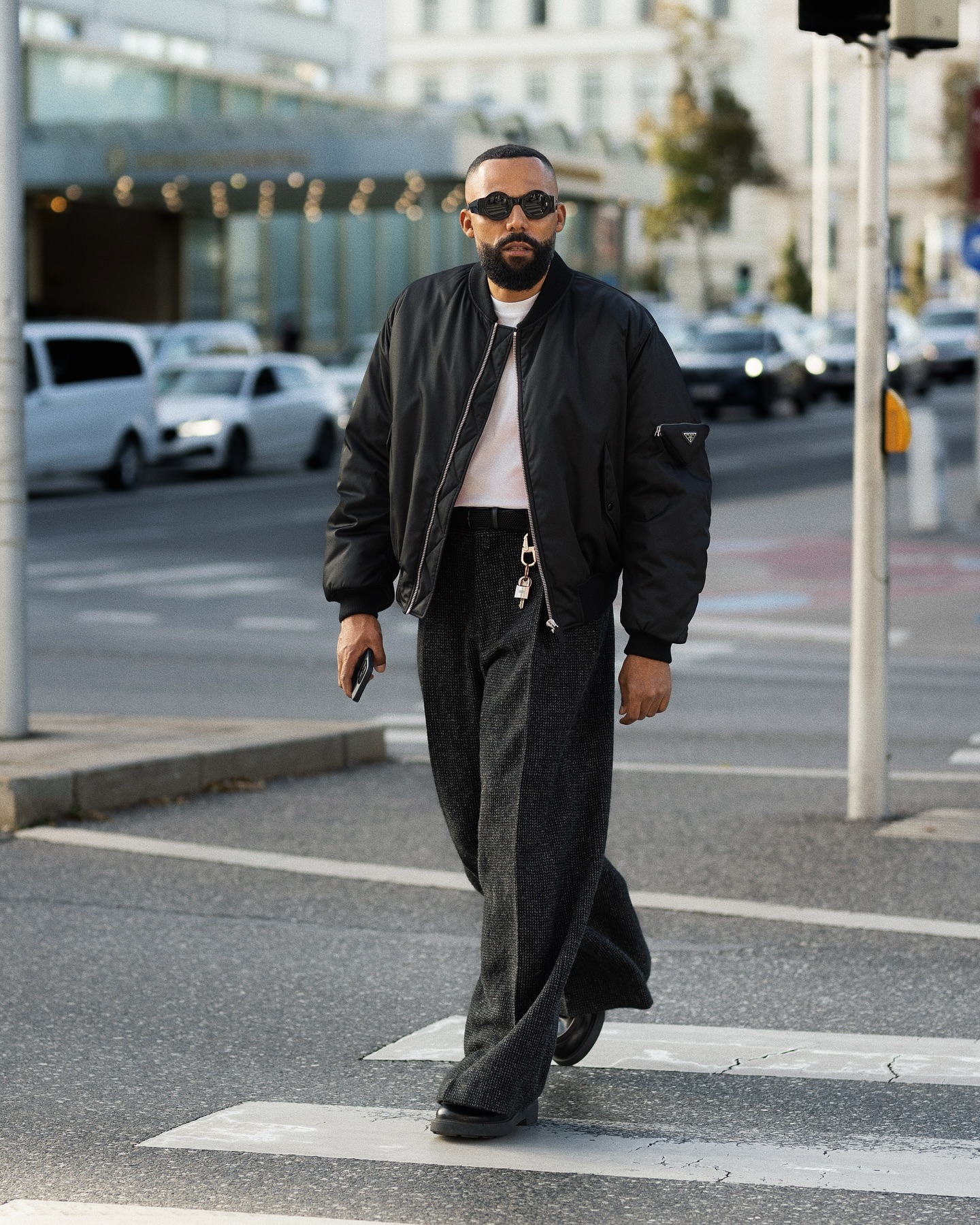 Jean-Claude Mpassy wears a black Prada bomber over a white shirt with wide charcoal trousers and black shoes