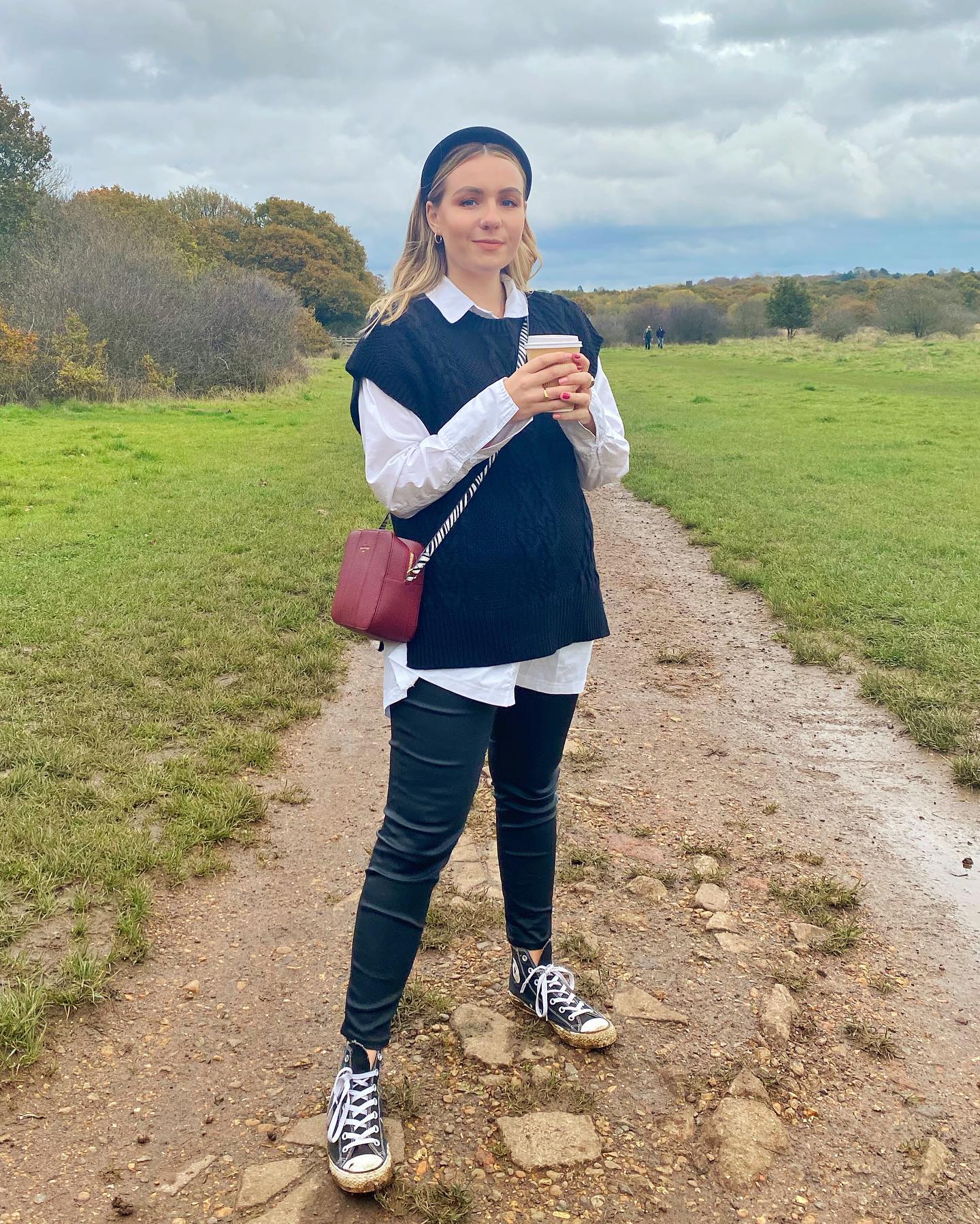Woman wearing a white button-up under a dark sweater vest with fitted trousers and sneakers