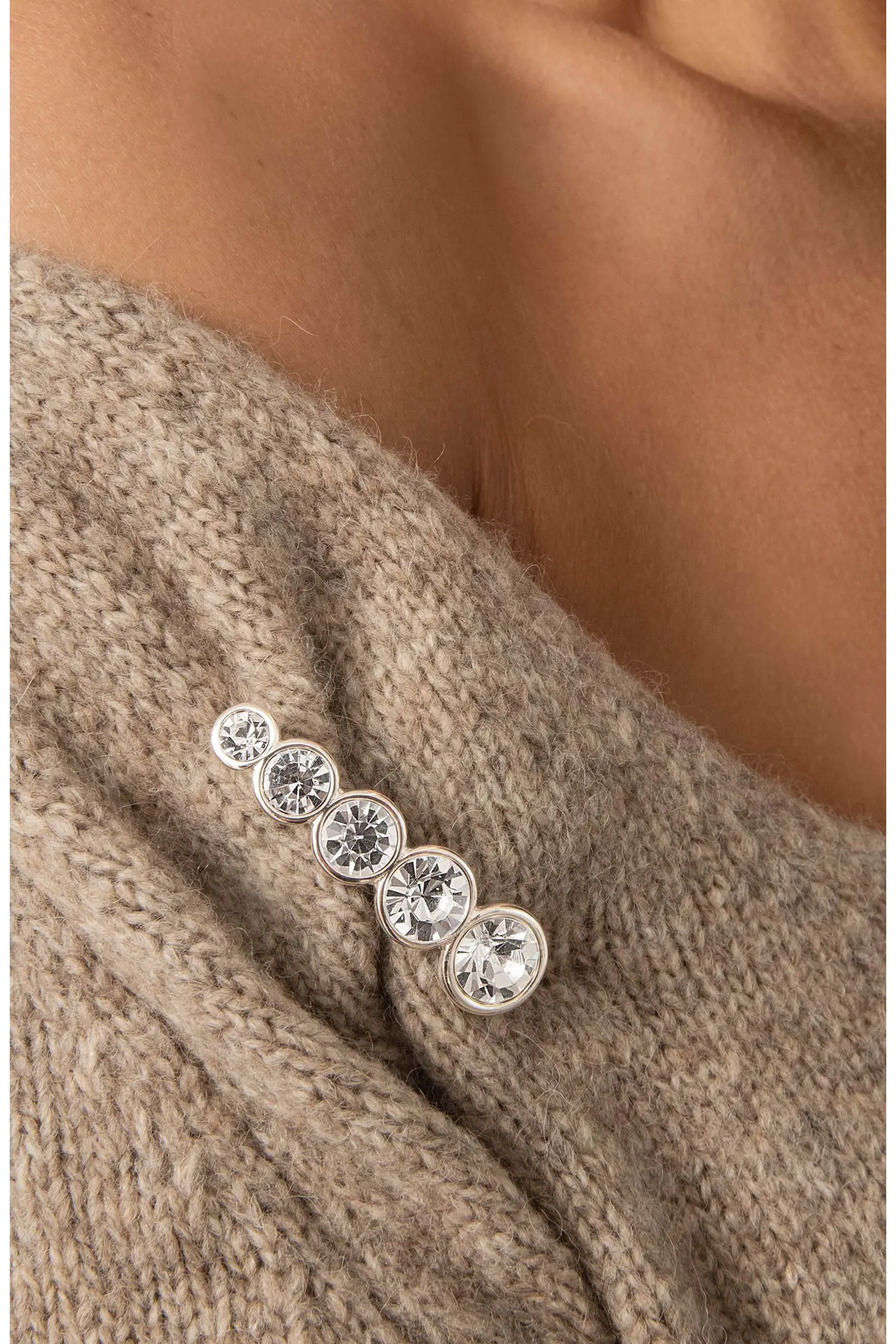 Ettika graduated crystal line brooch pinned to a taupe knit