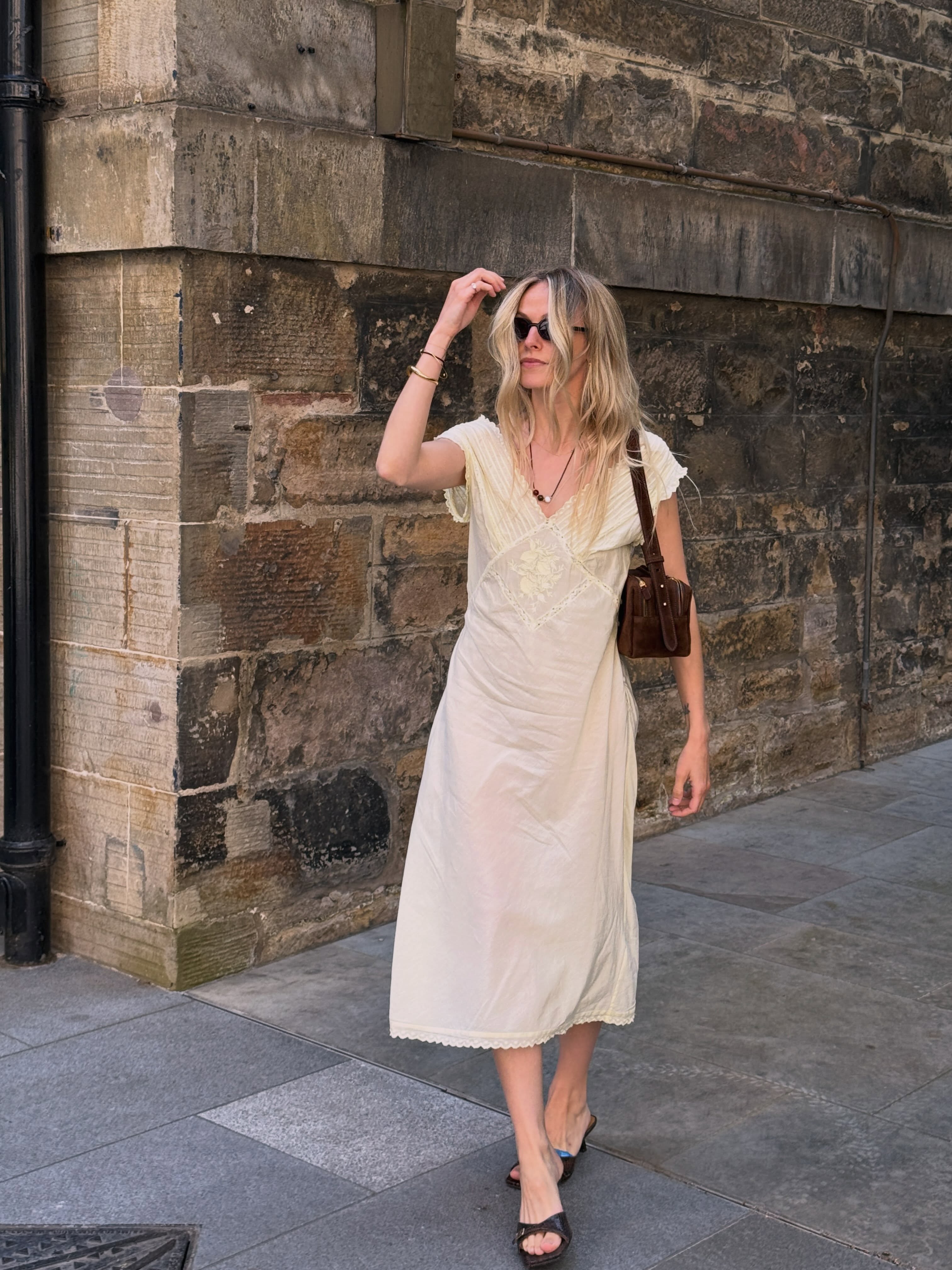 Jo-Ann Alari in a white summer dress with a brown shoulder bag and black sandals