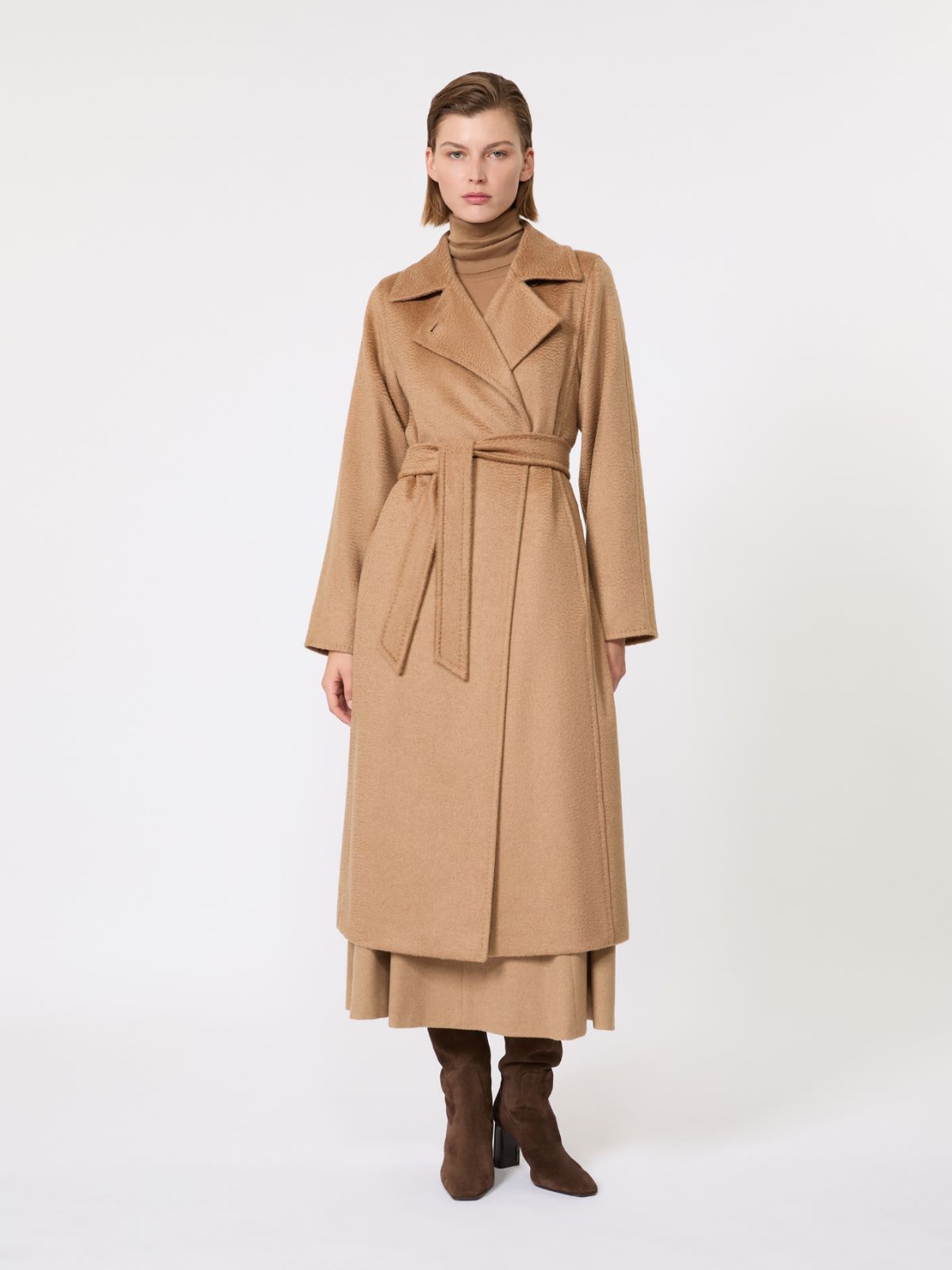 Max Mara Manuela Icon Coat on a model, tan belted wrap shape, wide lapel, long hem, and soft camelwool texture visible.