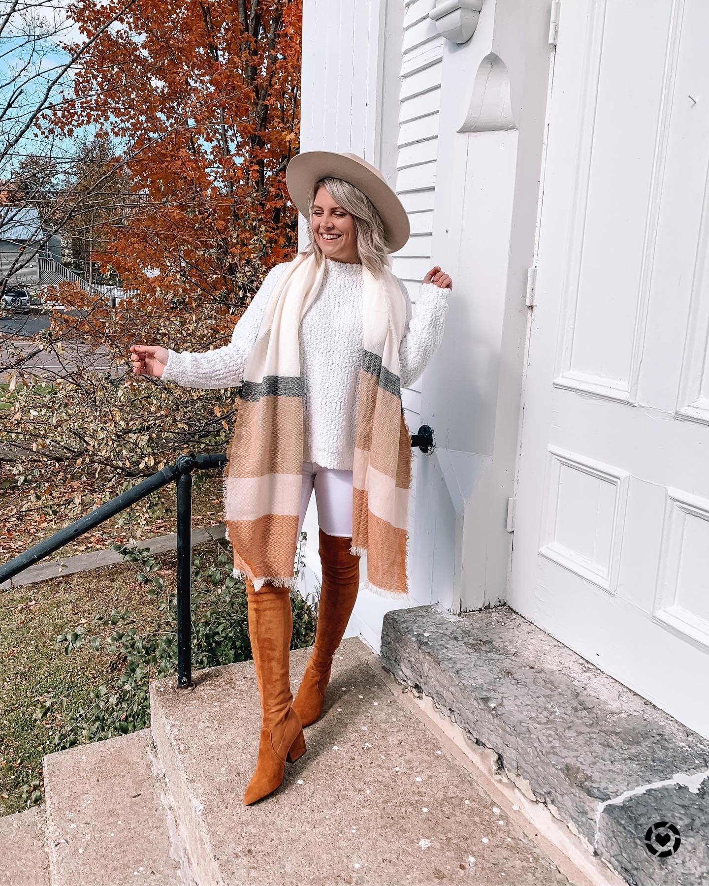 Woman in a white textured sweater and neutral scarf with brown over-the-knee boots
