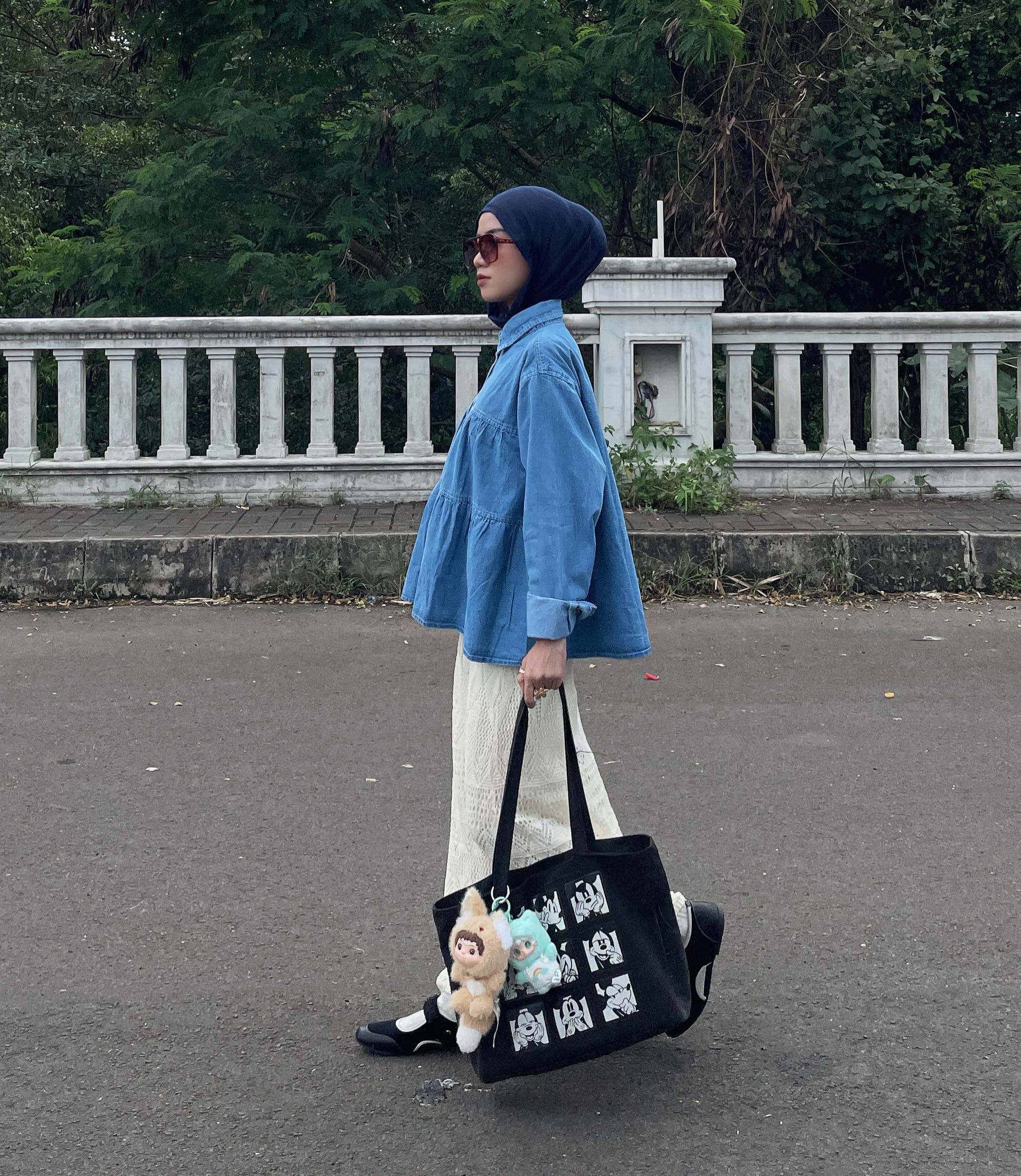 Delia in a tiered blue denim peplum shirt, a long white skirt, and black shoes