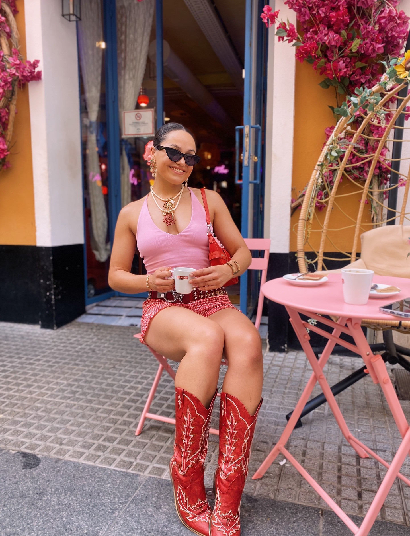 Fashion blogger in a pink tank and shorts with red cowboy boots and a red shoulder bag