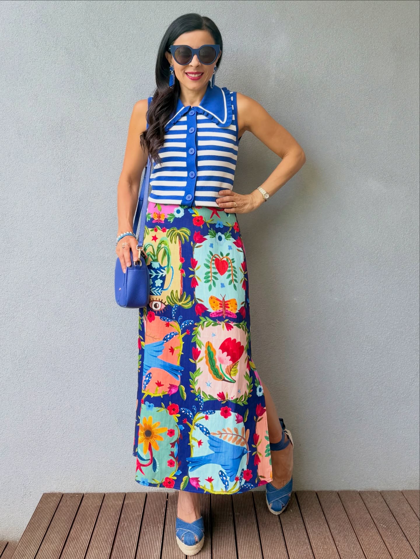 Woman in a blue-and-white striped sleeveless top and a colorful botanical-print maxi skirt with blue shoes