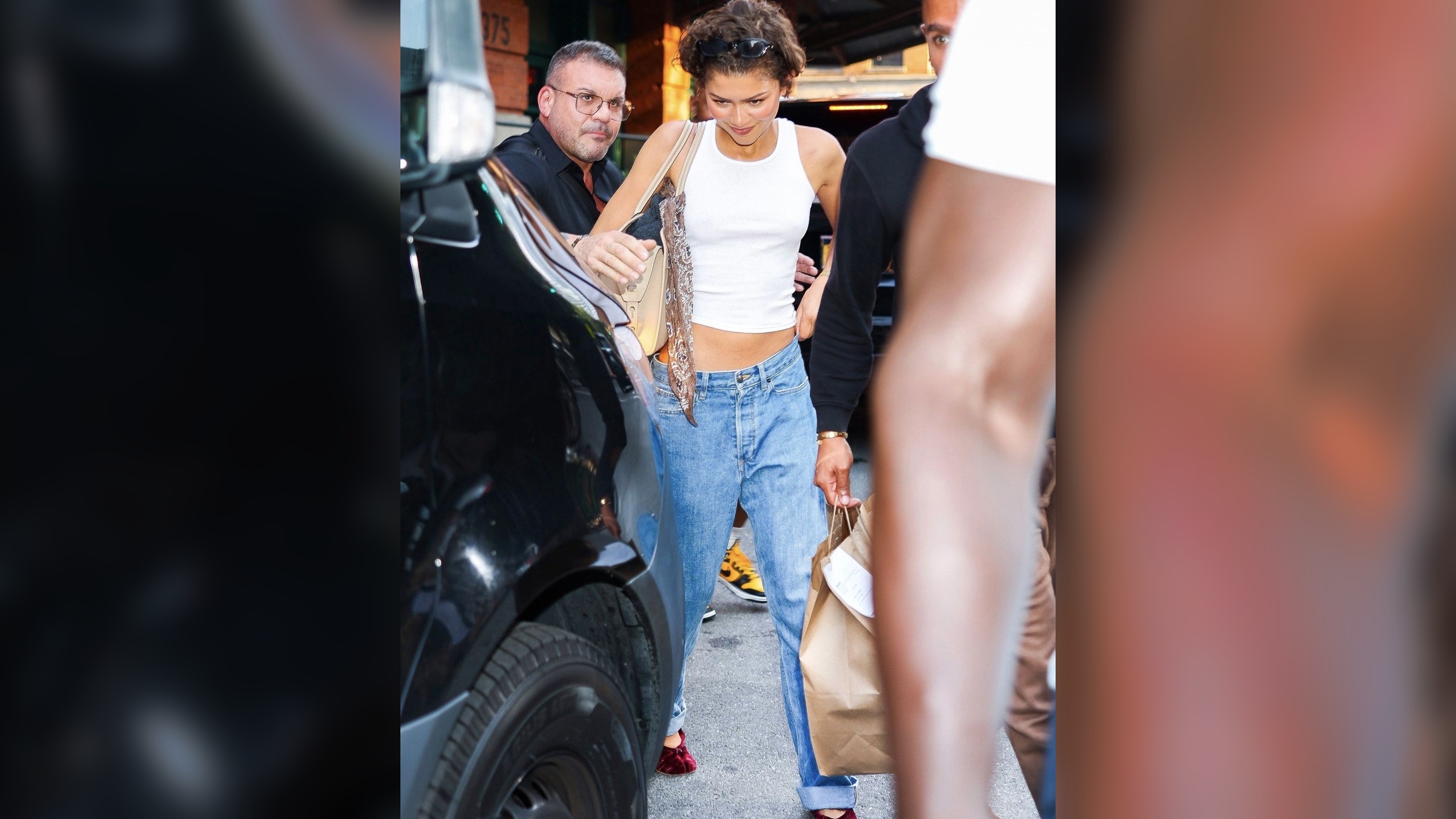 Zendaya in a white ribbed tank, relaxed blue jeans, and burgundy velvet ballet flats in New York