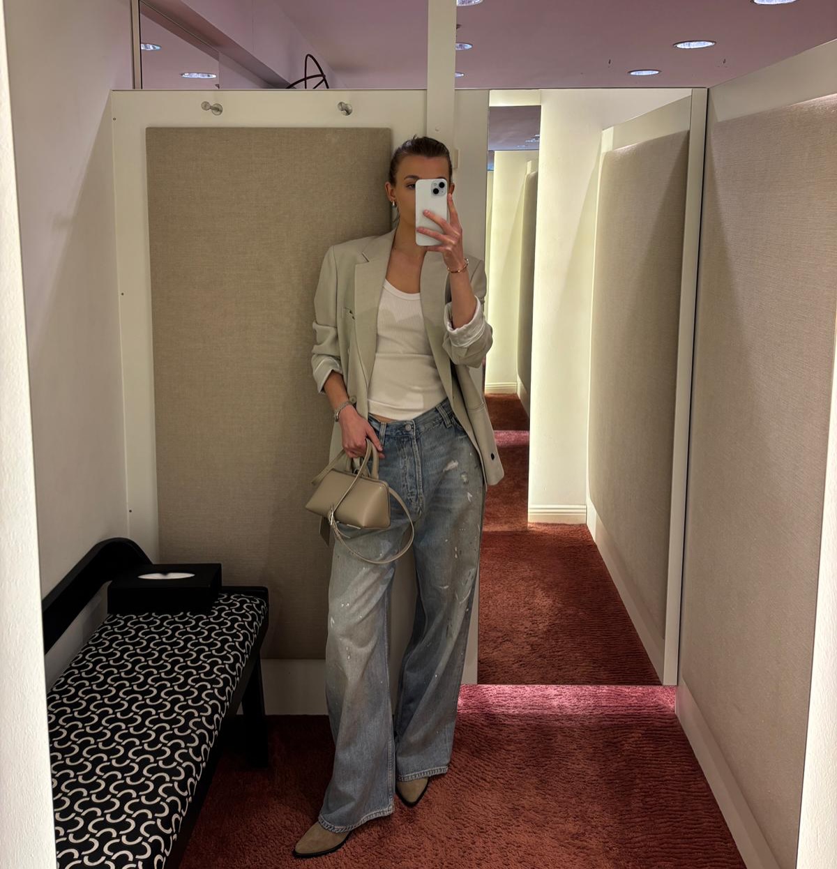 Woman styling wide light-wash Acne Studios jeans with a neutral blazer and pointed boots