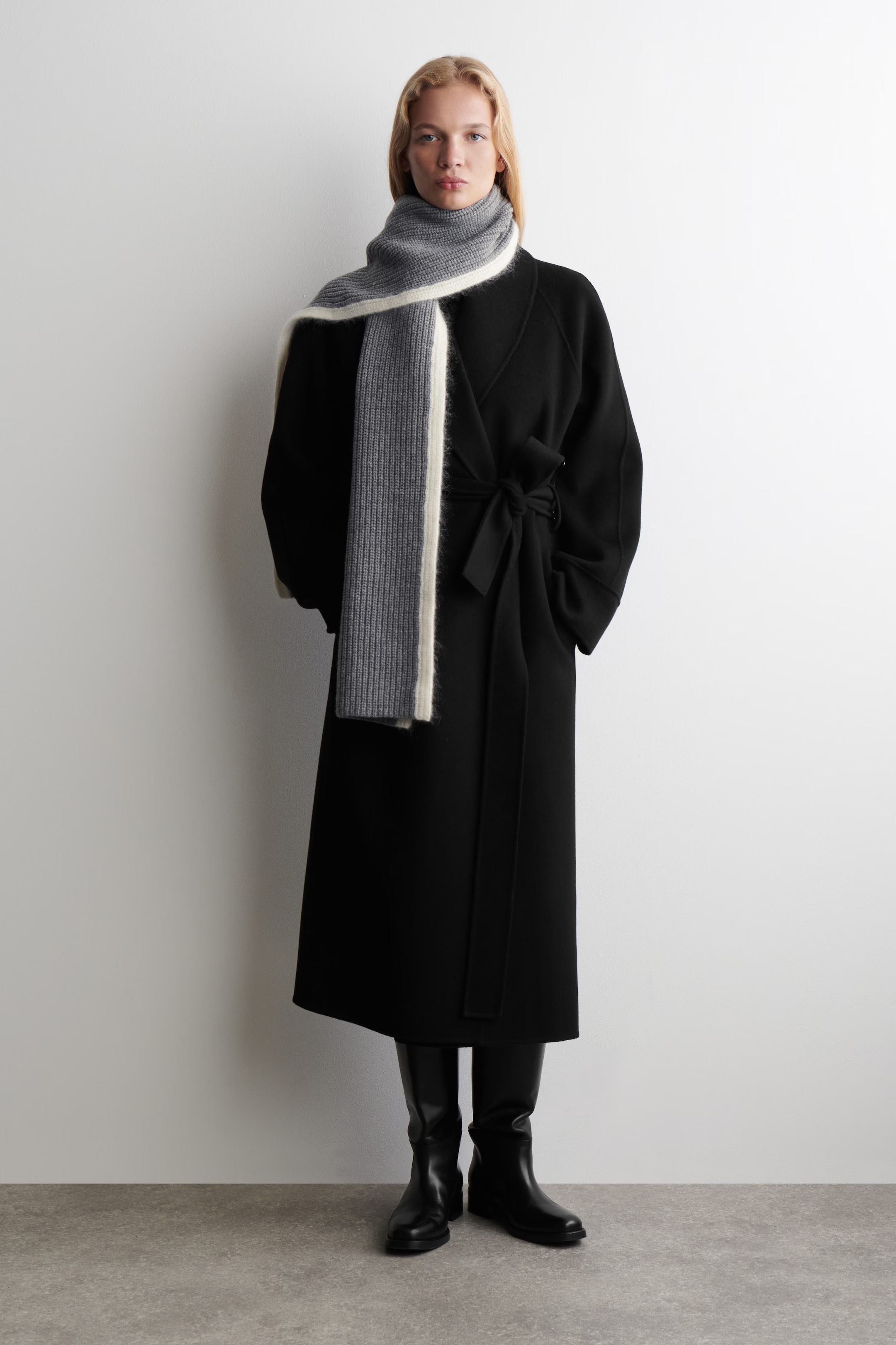 A model in a long black coat wears a chunky grey and cream wool mohair scarf in a high loop with a long front tail