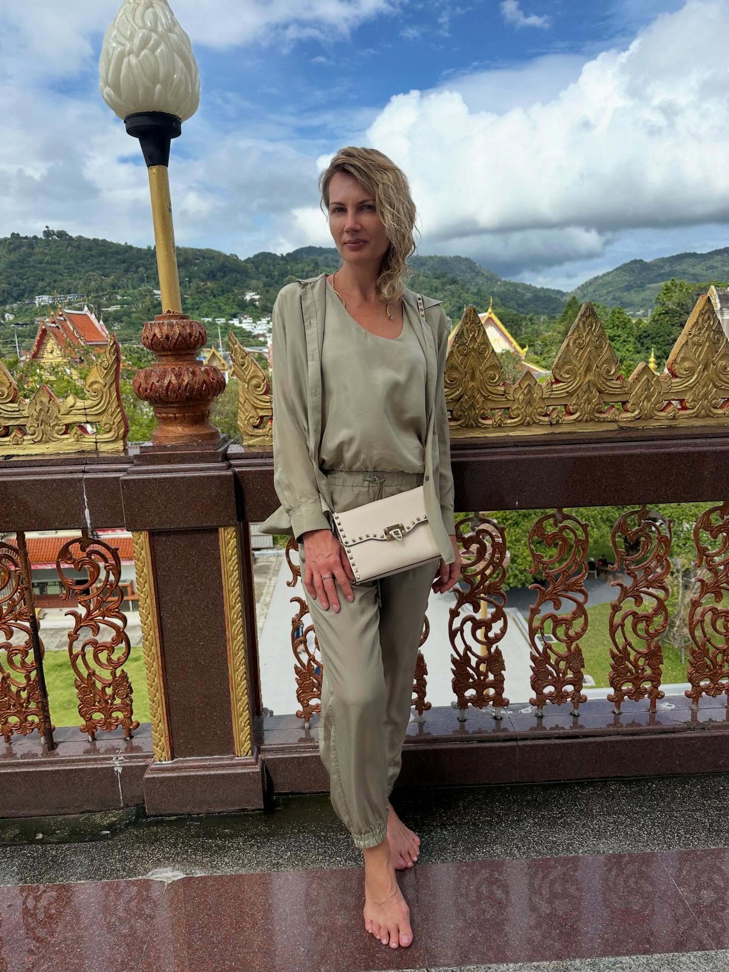 Woman wearing a pale olive satin jacket and top with relaxed olive trousers and a cream bag