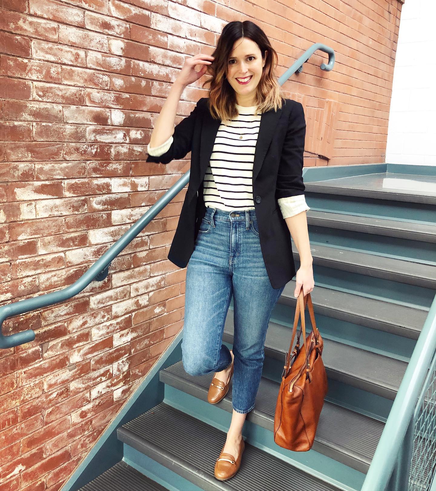 Woman wearing a black blazer, striped tee, cropped jeans, tan flats, and a brown tote